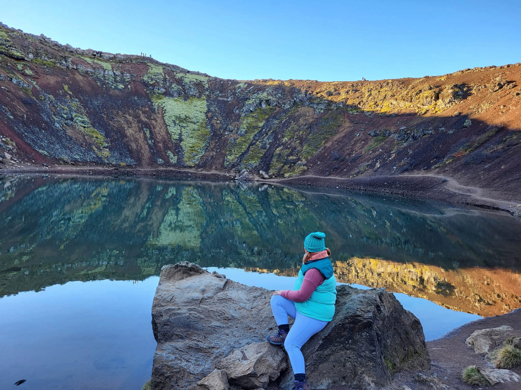 Katie of Wonderbound Travel wearing a blue beanie and overlooking a still volcanic crater lake in Iceland